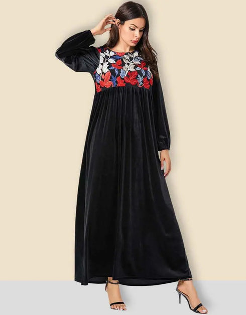 A flowing black or emerald green velvet abaya with delicate gold embroidery around the cuffs and neckline