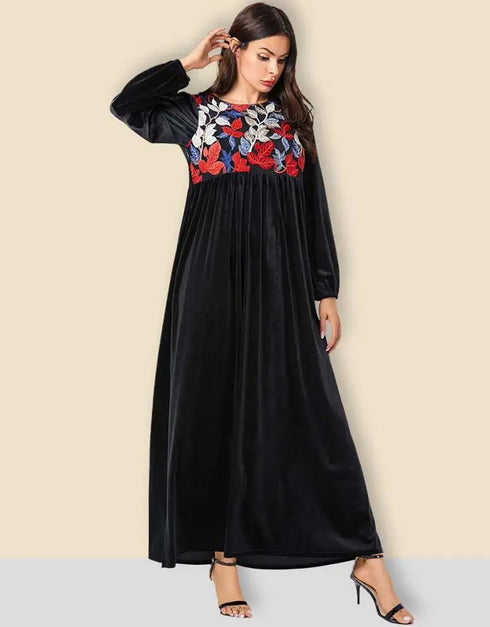 A flowing black or emerald green velvet abaya with delicate gold embroidery around the cuffs and neckline